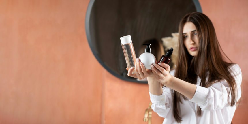 A beautiful brunette girl holds tubes of cosmetic products for hair and skin care. Copy space.