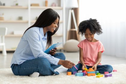 Adorable black kid and child psychotherapist playing with bricks