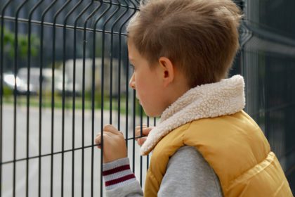 Portrait of upset little boy feeling alone looking through metal fence