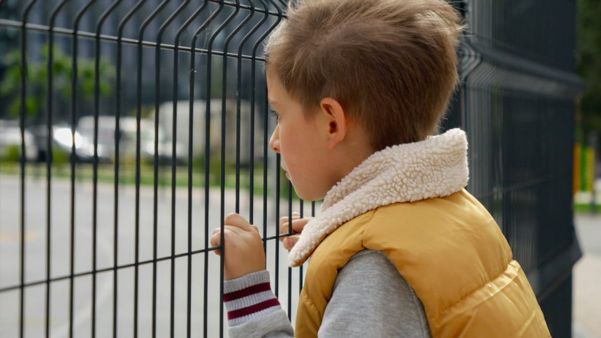 Portrait of upset little boy feeling alone looking through metal fence